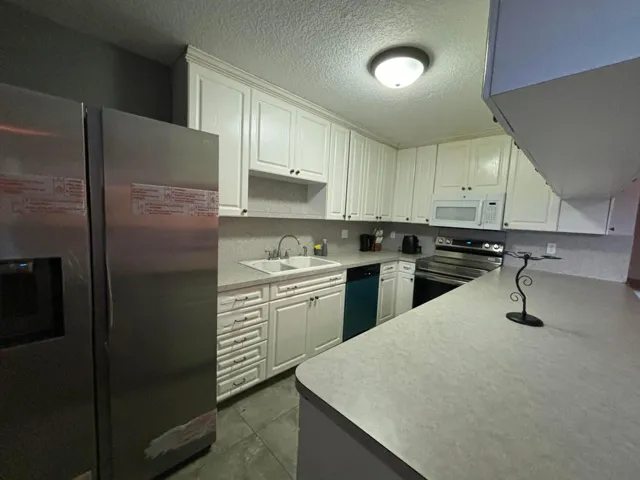 Contemporary kitchen featuring white cabinetry with dark hardware, a double basin sink, and integrated stainless steel appliances including a refrigerator, range, and microwave
