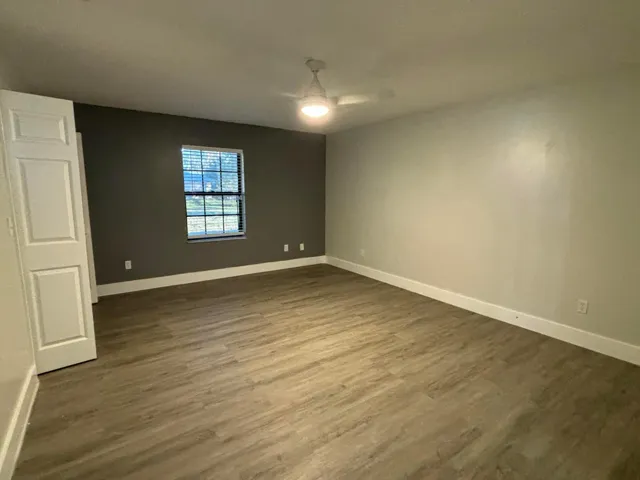 Spacious room featuring wood-finish flooring, a contemporary ceiling fan with integrated lighting, and a window with horizontal blinds