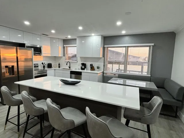 Modern kitchen featuring a large center island with a white countertop, stainless steel appliances, white flat-panel cabinetry, recessed lighting, and wood-finish flooring