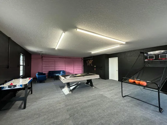 Spacious recreation room featuring grey carpet flooring, black textured walls, and a light pink accent wall