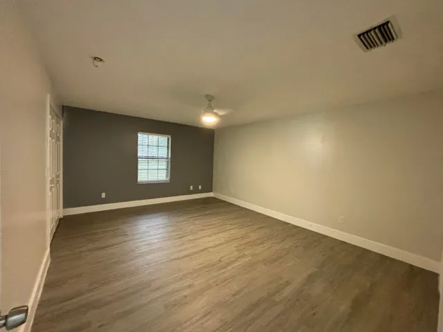 Spacious room featuring wood-finish flooring, a ceiling fan, and a single window with blinds