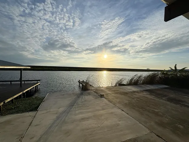 Waterfront property featuring a concrete boat ramp, two wooden docks, and mature waterside foliage
