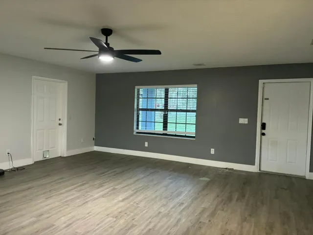 Spacious room featuring wood-finish flooring, a contemporary ceiling fan with integrated lighting, and a window with blinds