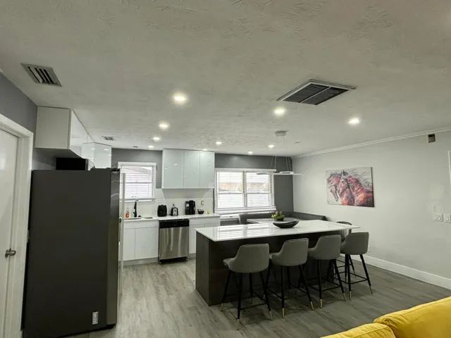 Contemporary kitchen featuring glossy white cabinetry, stainless steel appliances, a large island with seating, pendant lighting, and wood-finish flooring
