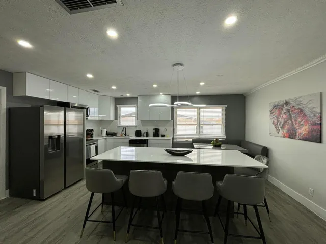 Contemporary kitchen featuring an oversized island with a white countertop, modern pendant lighting, stainless steel appliances, white flat-panel cabinetry, and wood-finish flooring