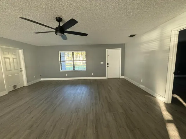Spacious room featuring wood-finish flooring, a modern black ceiling fan with integrated lighting, and neutral gray walls