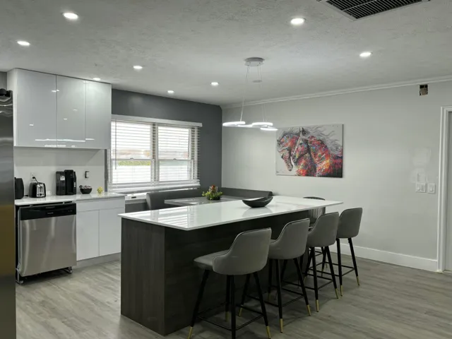 Modern kitchen featuring a spacious island with seating, white high-gloss cabinetry, stainless steel dishwasher, wood-finish flooring, and recessed lighting