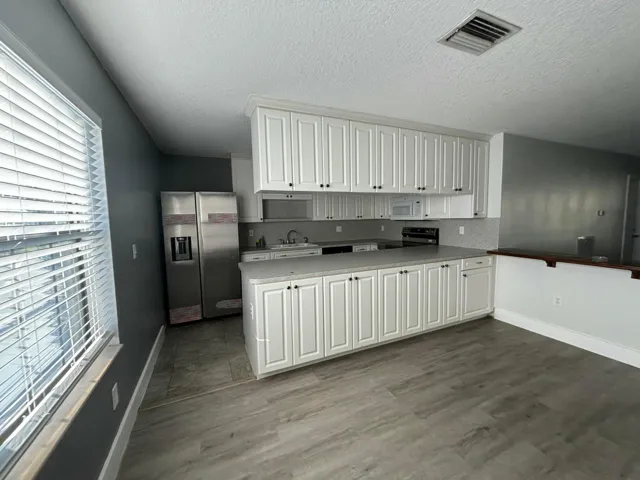 Kitchen featuring white shaker-style cabinetry, stainless steel appliances, grey wood-finish flooring, a light grey countertop, and a matching backsplash