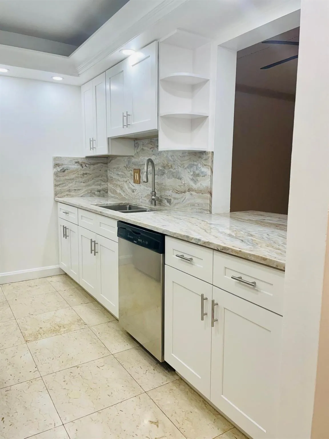 Kitchen featuring white shaker cabinetry, patterned stone countertops, a coordinating stone backsplash, a stainless steel dishwasher, and light tile flooring