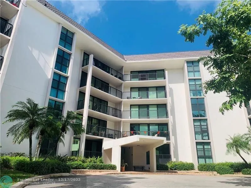 Multi-story building featuring a prominent front entrance with an overhang, multiple balconies with dark railings, and tall window banks