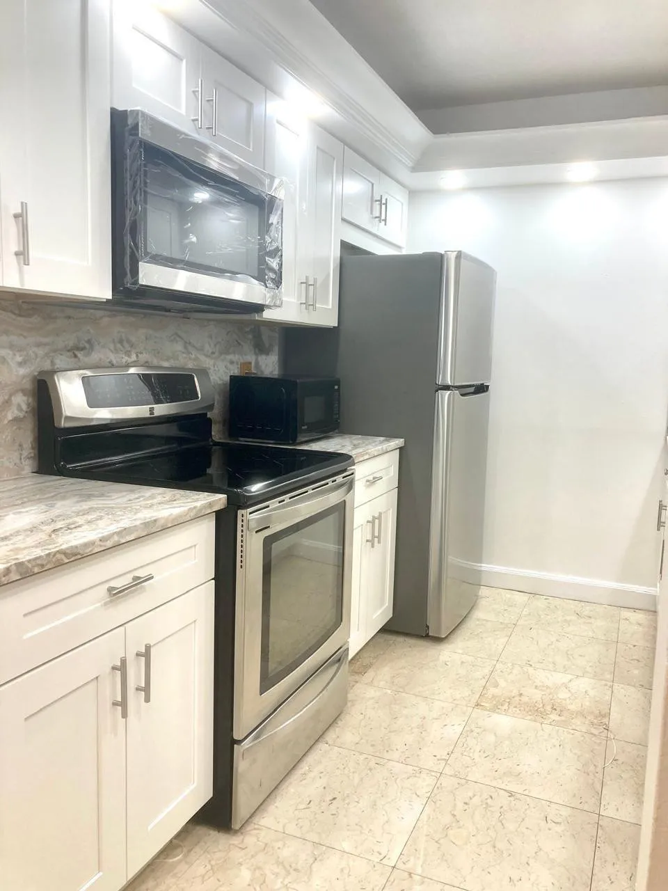 Kitchen featuring white shaker-style cabinetry, granite-finish countertops, tile flooring, and stainless steel appliances including a refrigerator, range, and built-in microwave