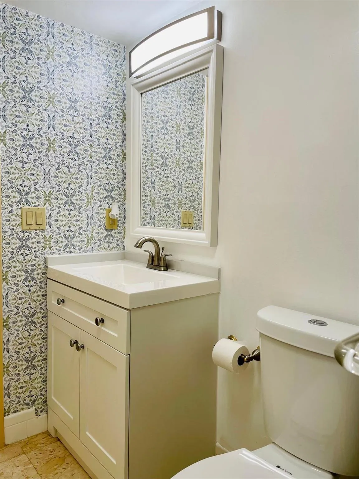 Bathroom featuring a vanity with a white countertop and integrated sink, brushed bronze faucet, and a wall-mounted mirror with an overhead light fixture