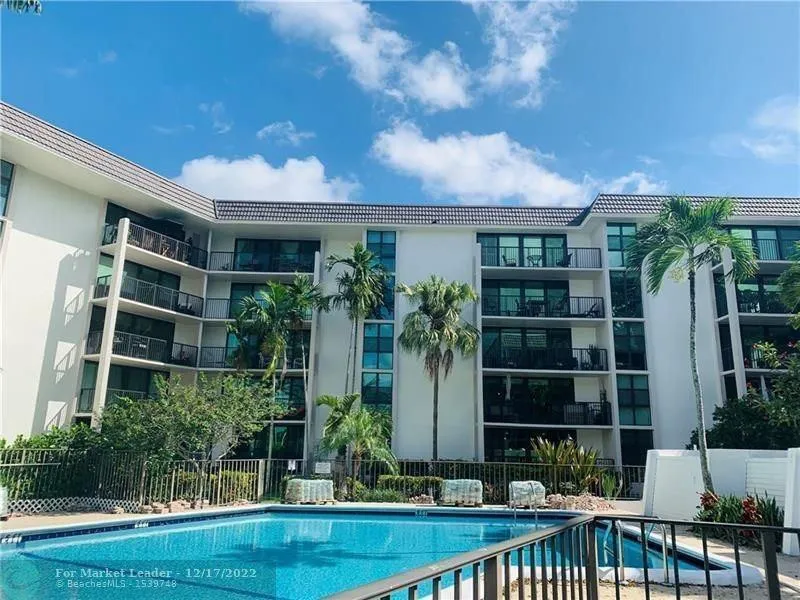 Community pool with a dark tile finish and adjacent white exterior multi-story building featuring multiple private balconies, dark-framed windows, and a tile roof