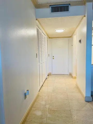 Entryway featuring square-format tile flooring, louvered bi-fold closet doors, a ceiling-mounted light fixture, and crown molding accents
