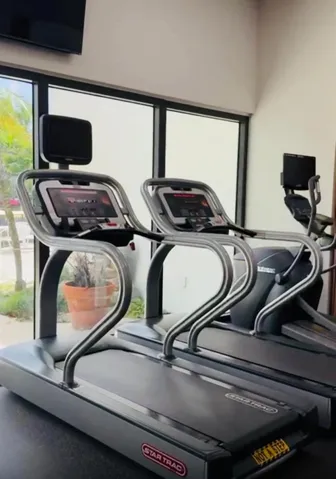 Fitness room featuring multiple treadmills, large floor-to-ceiling windows, and a wall-mounted television