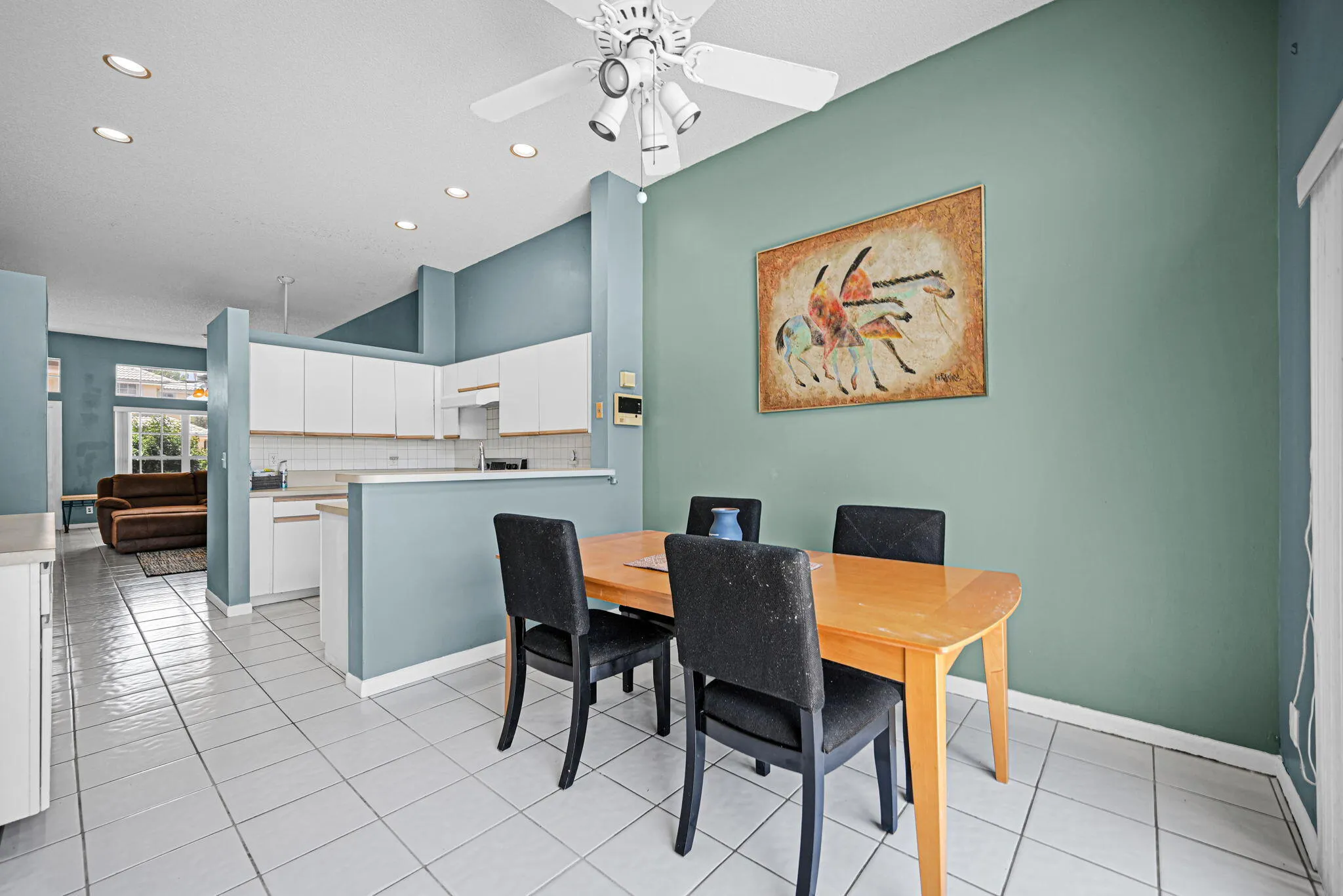 Kitchen and dining area featuring white tile flooring, vaulted ceilings, recessed lighting, and white cabinetry