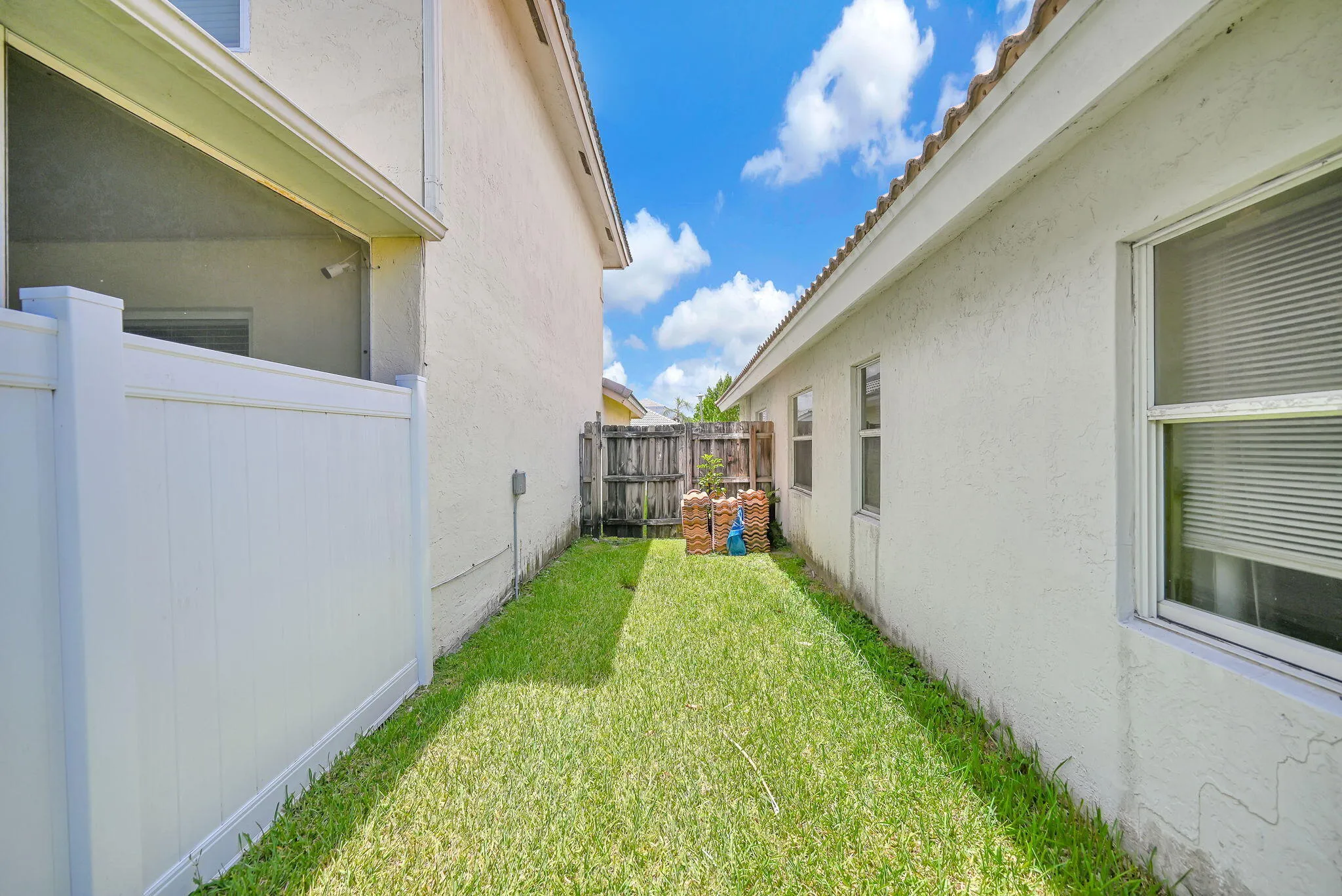 Grassed side yard featuring a white vinyl privacy fence, stucco exterior, and multiple windows