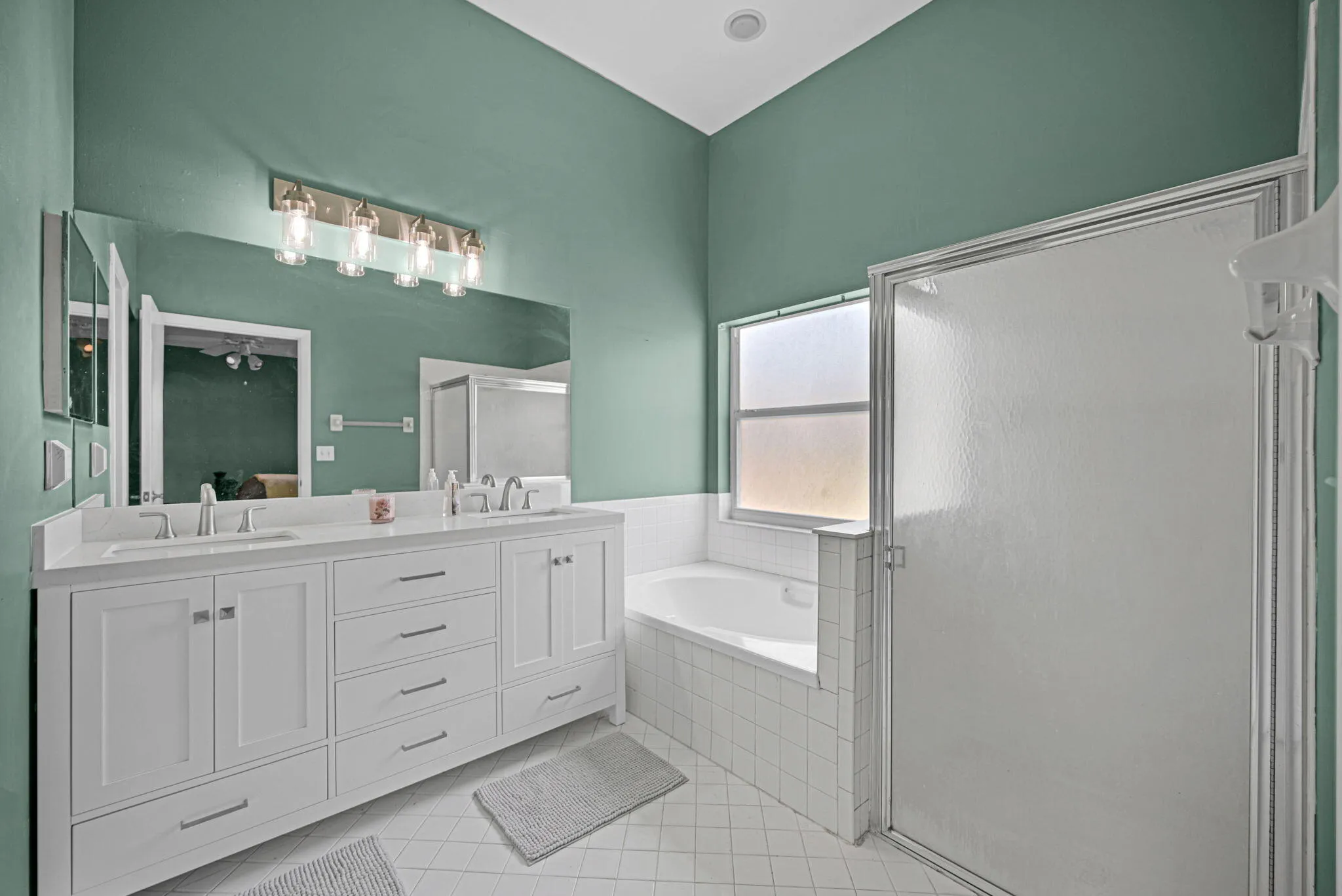 Double vanity with white cabinetry and chrome fixtures, large mirror, tile flooring, built-in bathtub, and an enclosed shower with frosted glass