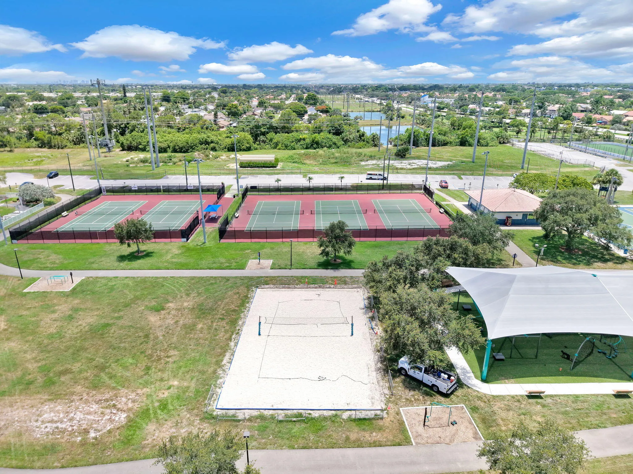 Aerial perspective showcasing multiple tennis courts, a sand volleyball court, and a large covered recreational area