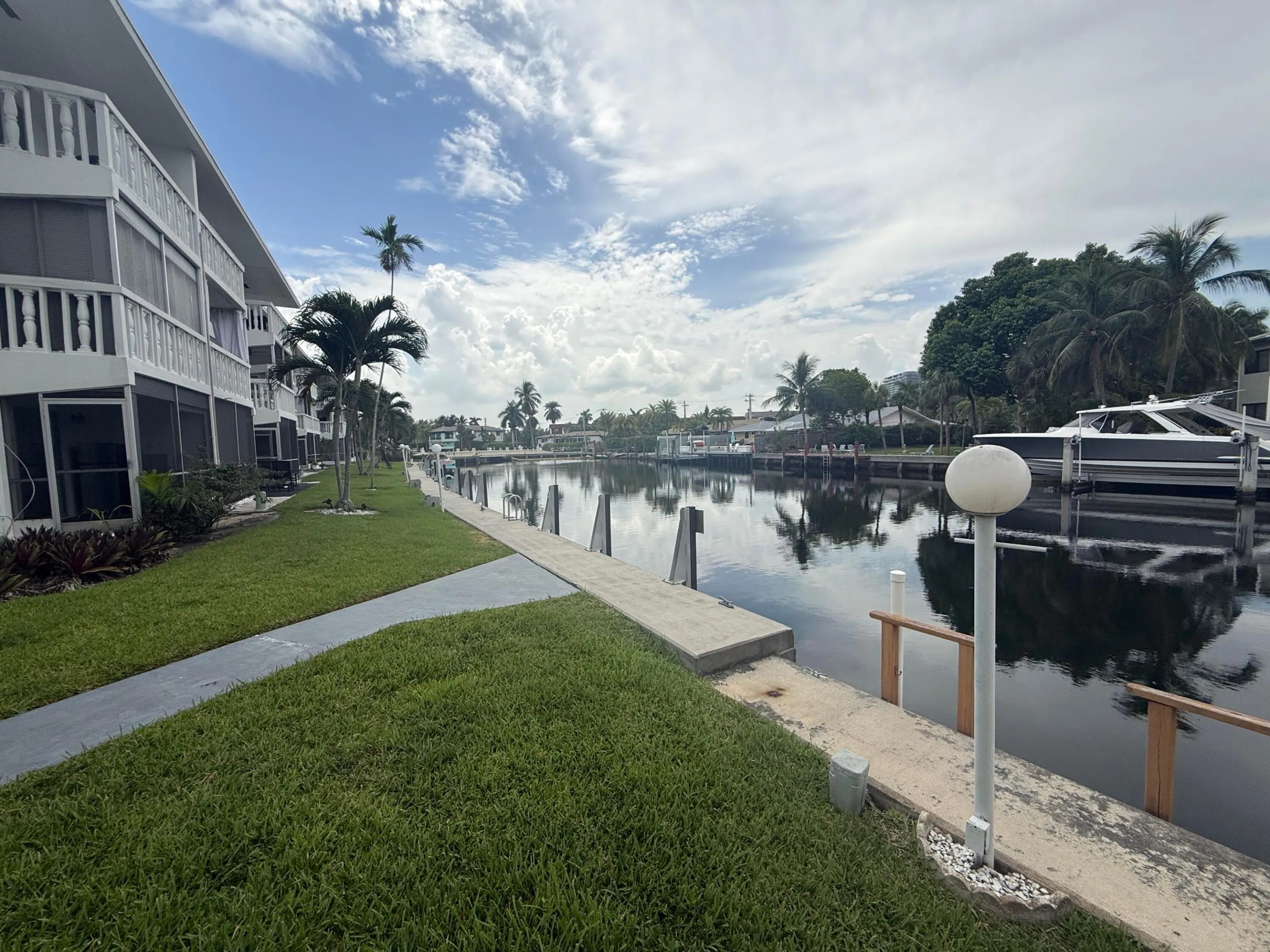 Waterfront property featuring a canal, mature palm trees, a concrete walkway, and a manicured lawn