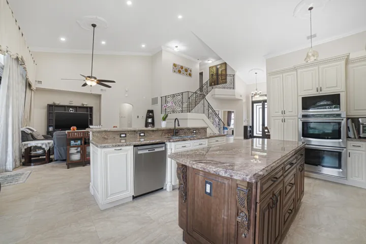 Gourmet kitchen featuring a large island with an integrated sink, stainless steel appliances including double ovens and a dishwasher, extensive light-toned cabinetry, and tile flooring