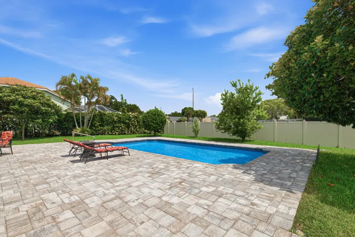 Rectangular swimming pool surrounded by a paver patio and green lawn