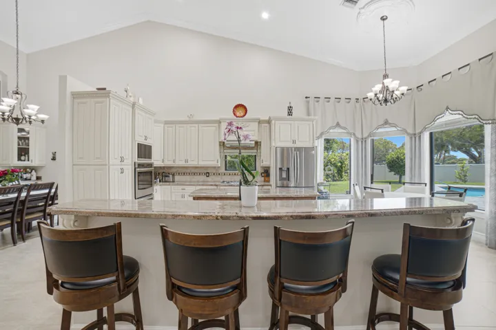 Kitchen featuring a large island with stone countertop, white cabinetry, integrated double oven, stainless steel refrigerator, and recessed lighting