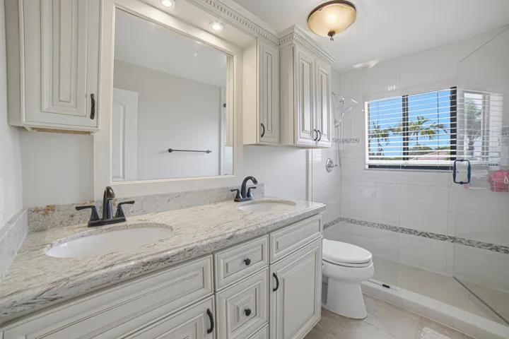 Bathroom featuring a double vanity with stone countertops, white shaker-style cabinetry, and matte black fixtures