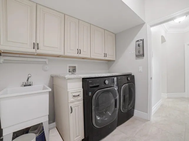 Functional utility room featuring extensive upper and lower cabinetry, a built-in sink, a light-toned countertop, and tile flooring
