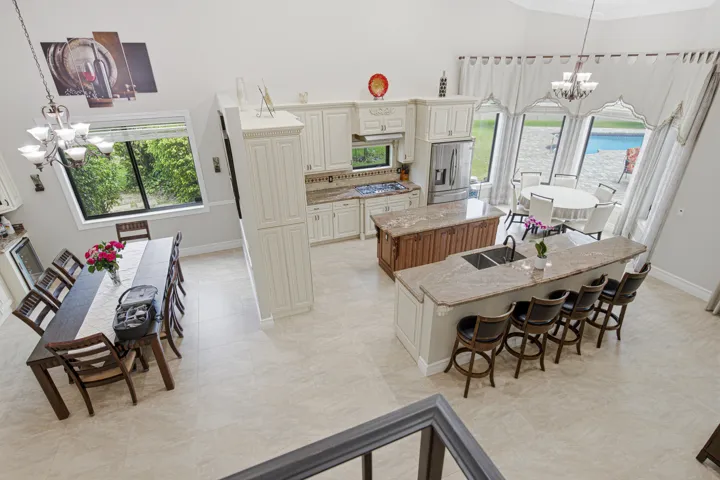 Open-concept kitchen and dining area featuring light-toned tile flooring, tall white cabinetry, a large kitchen island with seating, a secondary island with a wood-finish base, and a dining table
