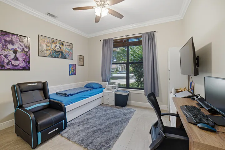 Room featuring tile flooring, a ceiling fan with integrated lighting, crown molding, a window with horizontal blinds and drapes, and a built-in desk with shelving