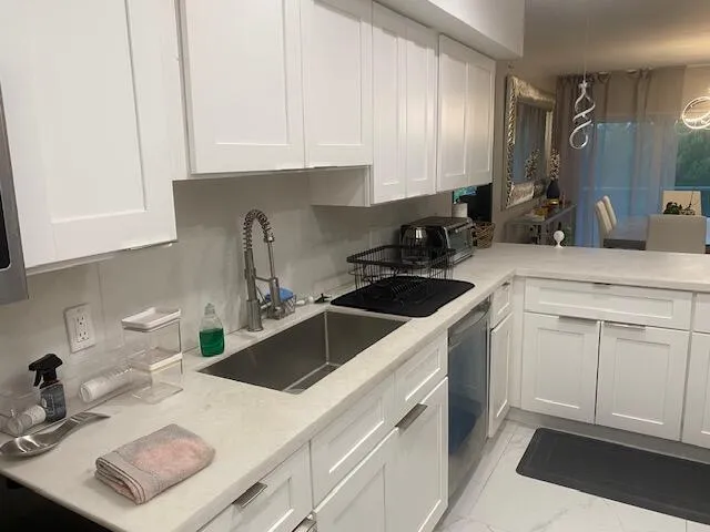 Modern kitchen featuring white shaker-style cabinetry, light-toned countertops, and a stainless steel undermount sink with a gooseneck faucet