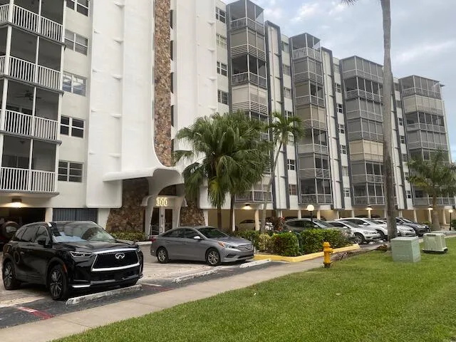 Multi-story residential building featuring white exterior, decorative stone facade, and numerous screened balconies