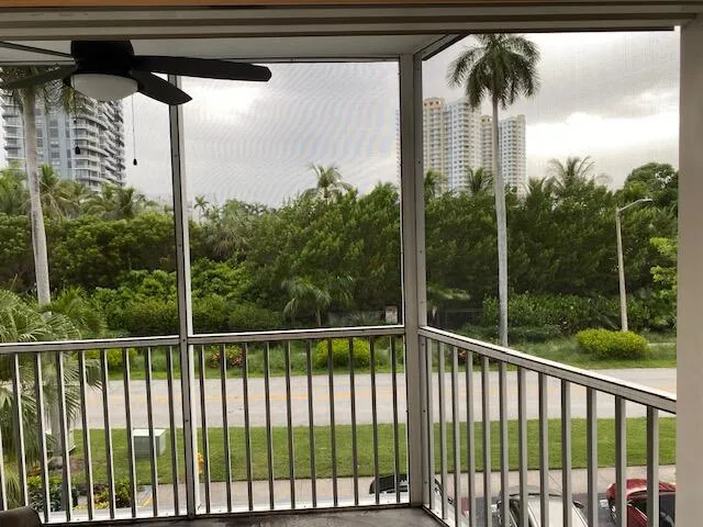 Screened balcony featuring a ceiling fan, white railings, and a tropical landscape backdrop