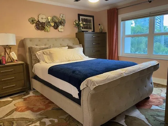 Bedroom featuring a window with exterior tree and building scenery, a ceiling fan with integrated lighting, and crown molding