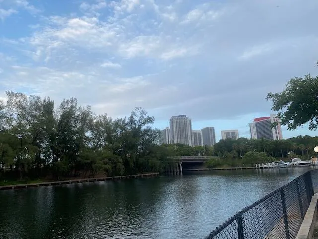 Waterfront property featuring a canal, mature trees, and a city skyline backdrop