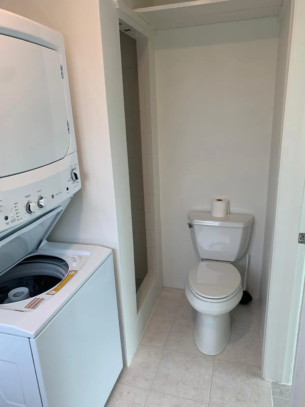 Laundry area featuring a stacked washer and dryer, tile flooring, and a commode
