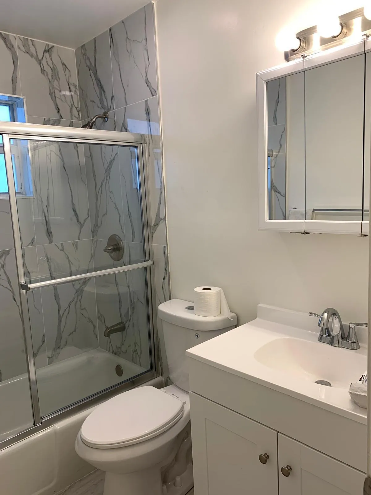Bathroom featuring a white vanity with integrated sink, chrome faucet, and a wall-mounted medicine cabinet with a three-light fixture