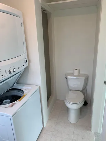 Laundry area featuring a stacked washer and dryer, tile flooring, and a commode