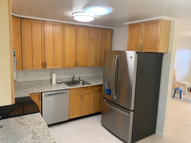 Kitchen featuring light wood cabinetry, light speckled countertops, stainless steel sink, and a tile backsplash