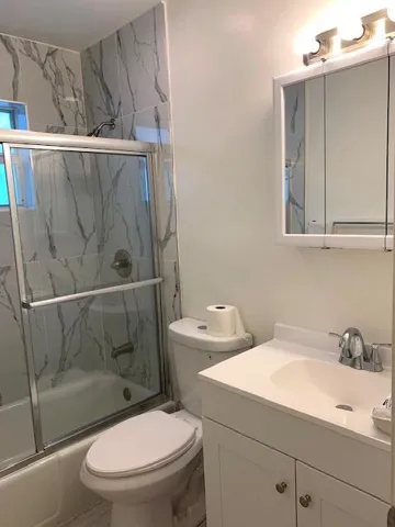 Bathroom featuring a tub/shower combination with sliding glass doors, white vanity with integrated sink, chrome faucet, and a wall-mounted medicine cabinet