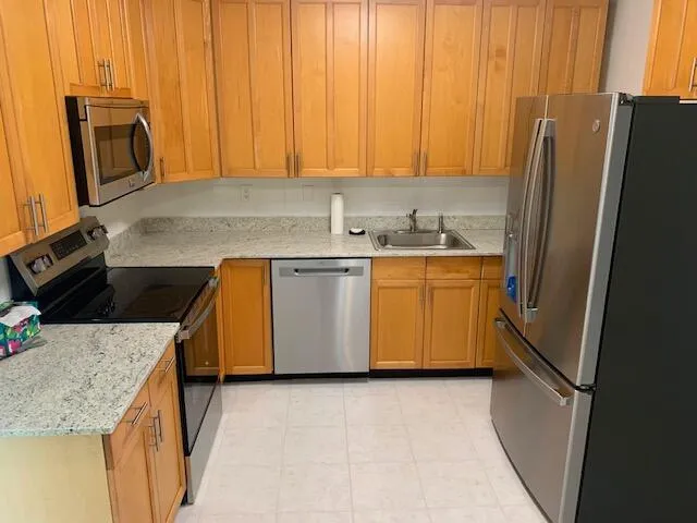 Kitchen featuring wood cabinetry, light-toned countertops, and stainless steel appliances including a refrigerator, dishwasher, microwave, and range