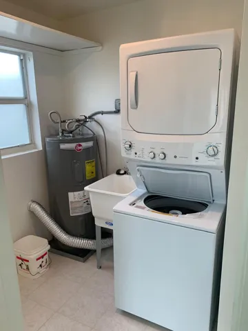 Dedicated laundry area featuring a stackable washer and dryer, utility sink, water heater, and a window for natural light