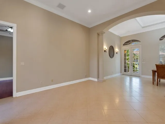 Living room featuring french doors, arched walkways, crown molding, ornate columns, and light tile patterned floors