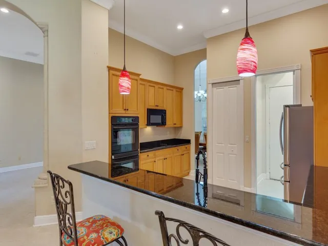 Kitchen with crown molding, a kitchen breakfast bar, decorative light fixtures, light tile patterned flooring, and dark stone countertops