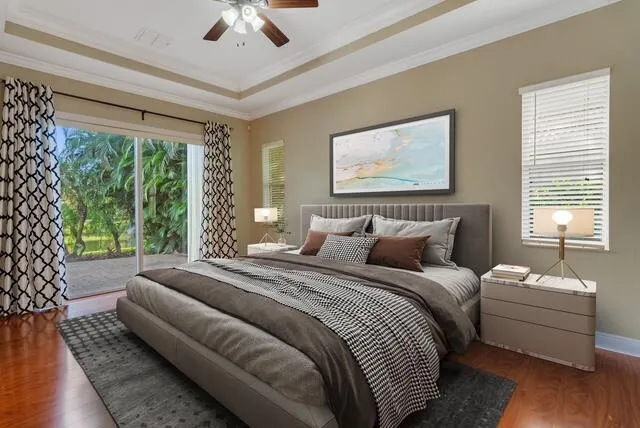 Bedroom with access to exterior, dark wood-style flooring, a tray ceiling, crown molding, and ceiling fan