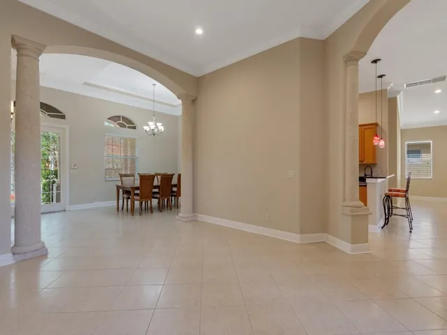 Living room featuring decorative columns, arched walkways, crown molding, recessed lighting, and a chandelier