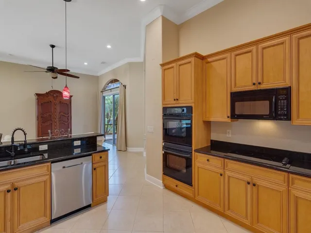 Kitchen with crown molding, a kitchen breakfast bar, decorative light fixtures, light tile patterned flooring, and dark stone countertops
