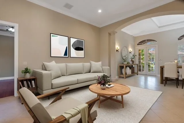 Living room featuring french doors, arched walkways, crown molding, ornate columns, and light tile patterned floors