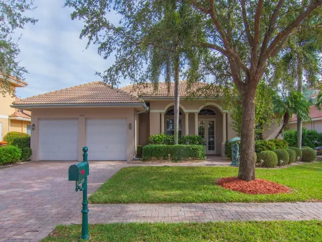 View of front facade with stucco siding, a front yard, decorative driveway, a tiled roof, and a garage